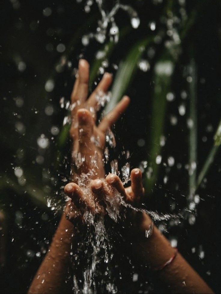 Hands under running water in tropical greenery